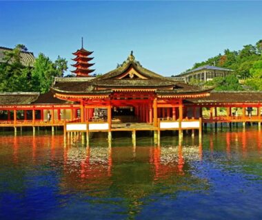Wooden shrine on stilts reflecting on calm water with pagoda backdrop near Miyajima Shiro, Hiroshima