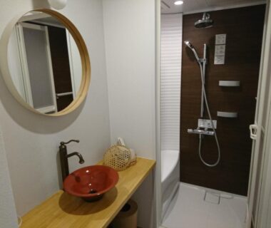 Compact bathroom with round mirror, red ceramic basin on wooden counter and adjacent shower at Miyajima Shiro, Hiroshima