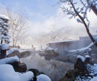 Steaming outdoor onsen surrounded by snow-covered rocks and trees at Miyama Ouan in Gifu Chūbu region