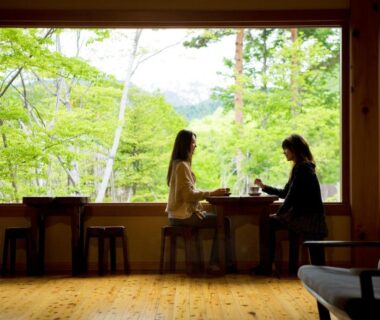 Two guests at wide window overlooking green forest, wooden interior seating at Miyama Ouan in Gifu
