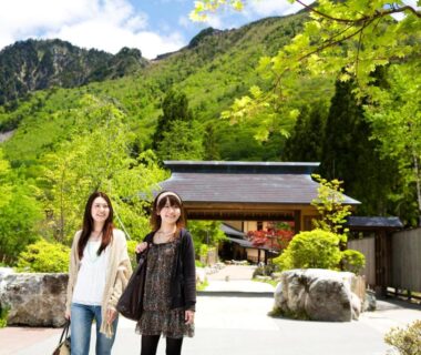 Two visitors walking toward Miyama Ouan entrance with green mountains and stone landscaping in Gifu