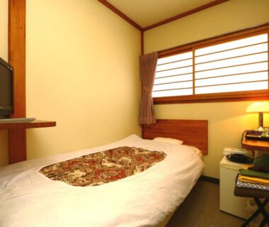 Small guest room with single bed, shoji window, wooden accents, TV and compact refrigerator at Miyamaso Gifu