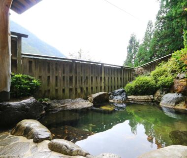 Outdoor rock lined onsen with wooden fence and mountain view at Miyamaso, Gifu