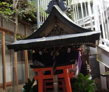 Compact Shinto shrine with red torii, shimenawa rope and stone basin beside stairwell at Miyoshiya Ryokan, Wakayama