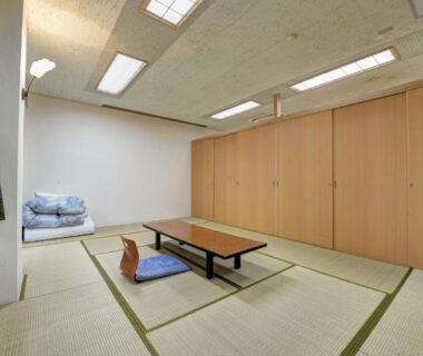 Tatami room with low table, zabuton cushions and stacked futon beside sliding wooden partitions at Mizu no Kaori in Kanagawa