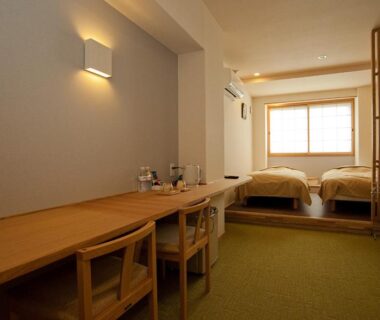 Twin beds on raised platform with wooden desk, shoji partition and green tatami flooring at Mizuhasou in Hiroshima