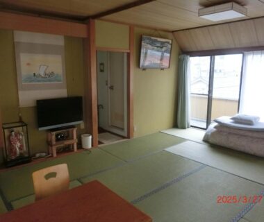 Tatami room with low table, stacked futon by balcony, wall scroll and TV at Mizuhokan in Mie