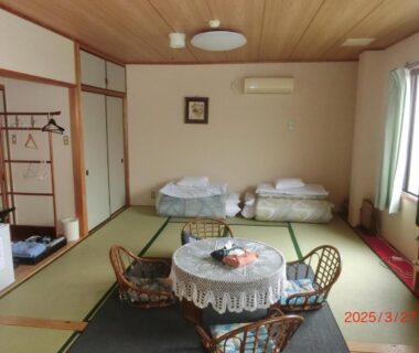 Tatami room with low table, lace cloth, futons and rattan chairs at Mizuhokan in Mie
