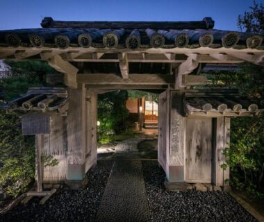 Night view of a lit wooden entrance gate and stone path leading into Mizuno Ryokan grounds in Saga, Kyushu