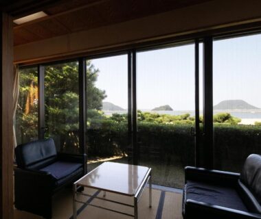 Tatami room with low table and seating, sliding glass doors opening to a hedged garden and distant coastal islands
