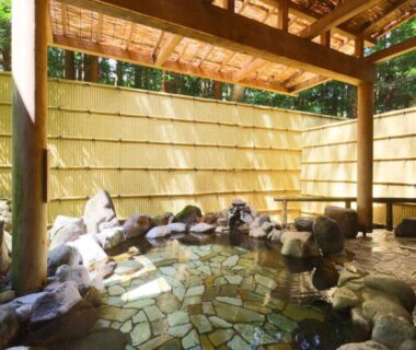 Stone-lined open-air onsen with wooden roof and bamboo fence at Mizunoto in Kanagawa