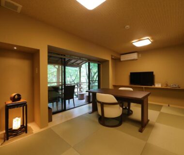 Tatami room with low table, comfortable chair, TV and terrace opening to green garden at Momijiya Annex Kyoto