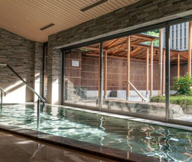 Indoor onsen bath with stone wall and garden courtyard visible through sliding glass at Monjusou, Kyoto