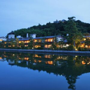 Riverside buildings lit at dusk reflecting on calm water, Monjusou ryokan, Kyoto Kansai