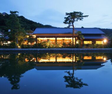 Evening pond reflection of Monjusou ryokan exterior with illuminated facade and trees, Kyoto, Kansai Japan