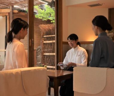 Guests and staff seated in serene wooden ryokan lounge at Monjusou Kyoto with garden view