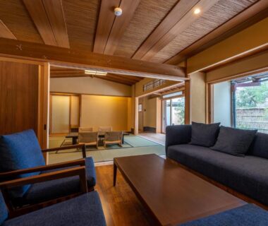 Spacious tatami room with low table, blue sofa, shoji screens and wooden ceiling at Monjusou Shourotei in Kyoto