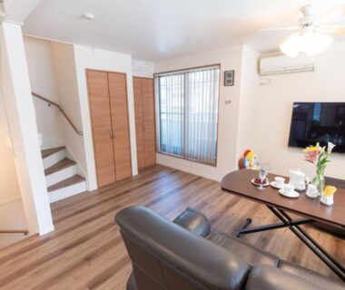 Compact living room with sofa, coffee table, TV and staircase at Mori House In 西日暮里I, Tokyo