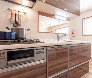 Gas stovetop, sink, and wooden cabinetry in compact kitchen at Mori House In 西日暮里I Tokyo