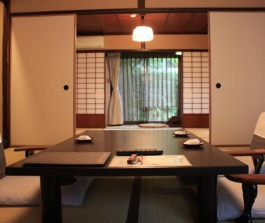 Traditional tatami room with low dining table, floor chairs, shoji screens and garden view at Motoyu Ishiya in Ishikawa