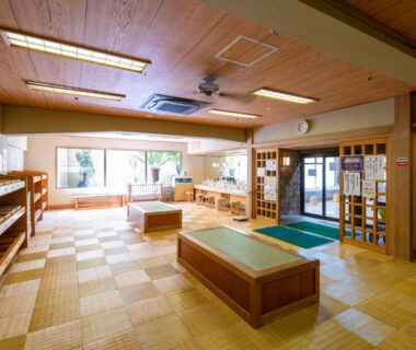 Spacious wooden ryokan lobby with tatami flooring, seating benches, shoe shelves and large front windows in Yamanashi