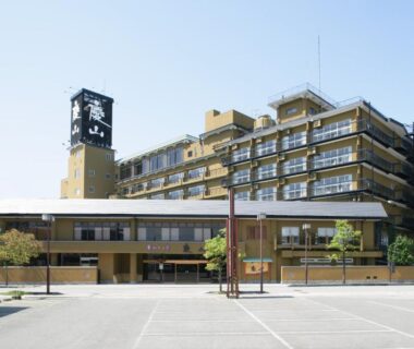 Multi-storey ryokan exterior with entrance canopy, balconies and parking area in Yamanashi