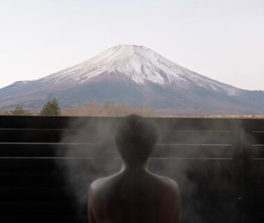 Silhouette in steaming bath with Mount Fuji visible beyond wooden railing, Yamanashi