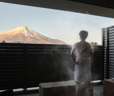 Person in towel by steaming balcony bath with Mount Fuji visible beyond wooden shutters at Ryokan Shizuku in Yamanashi