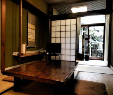 Traditional tatami room with low wooden table, shoji screens, tokonoma alcove and entrance to a small garden path