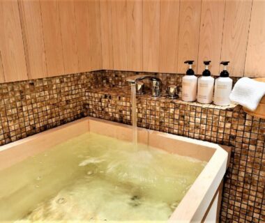 Indoor wooden soaking tub with mosaic tile surround and bath amenities at Muromachi Yutone Kyokoyado Kyoto