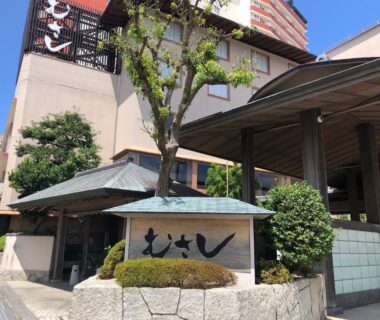 Exterior entrance with wooden canopy, stone wall, greenery and Musashi signboard in Wakayama