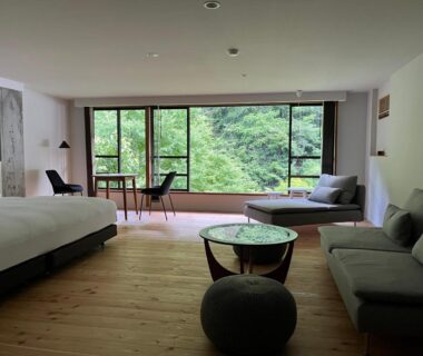 Spacious room with bed, sofa and floor-to-ceiling window overlooking forest at Myojinkan in Nagano, Chūbu, Japan
