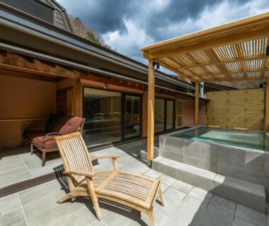 Outdoor soaking tub with wooden lounge chair and glass sliding doors at Myojinkan Nagano