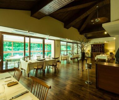 Spacious wood-floored dining area with table settings and large windows overlooking green garden at Myojinkan Nagano