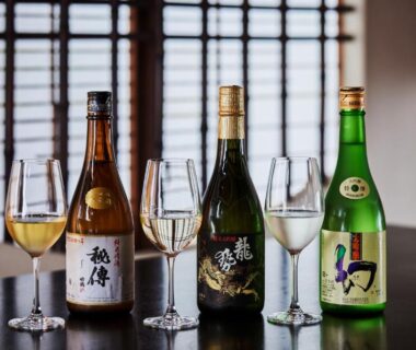 Three bottles with wine glasses on lacquered table by shoji screens at NIPPONIA HOTEL Takehara