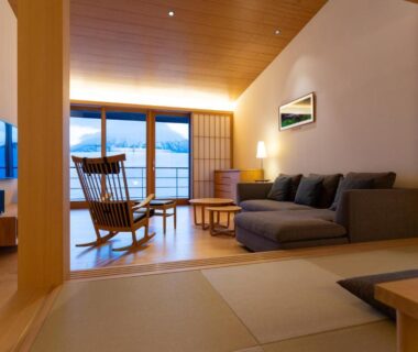 Tatami seating area with sofa and rocking chair opening onto balcony with mountain view in Hokkaidō