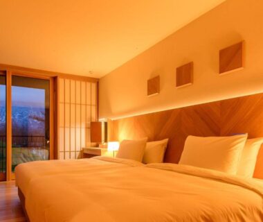 Warm-lit twin beds, wooden headboard, shoji screens and sliding glass doors to balcony at NISEKO Inn of Youtei, Hokkaidō