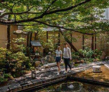 Two people walking on wooden path beside pond in Nishiyama Ryokan garden, Kyoto Kansai Japan