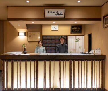 Two staff behind illuminated wooden reception counter at NISHIYAMA RYOKAN Established in 1953 Kyoto