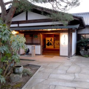 Stone path leading to Nagataki entrance with wooden beams, lantern and garden plants in Gifu