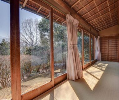 Tatami-lined engawa with wooden frames and glass sliding doors opening to a sunlit garden in Gifu