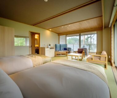 Bright tatami room with twin beds, low wooden ceiling, seating area and large windows at Nagisatei Taroan Iwate
