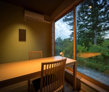 Wooden table and chairs beside large glass window overlooking a serene garden at Nagisatei Taroan, Iwate