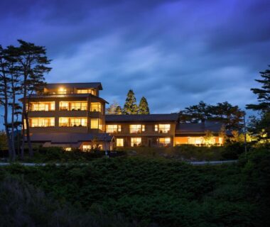 Multi-story lit ryokan building at dusk among trees and landscaped grounds in Iwate