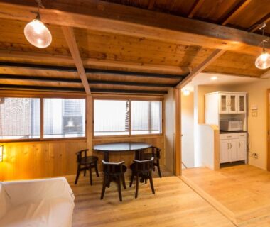 Interior with exposed wooden beams, low dining table, chairs, kitchenette and shoji screens at Nagomi-Ryokan Yuu in Kyoto