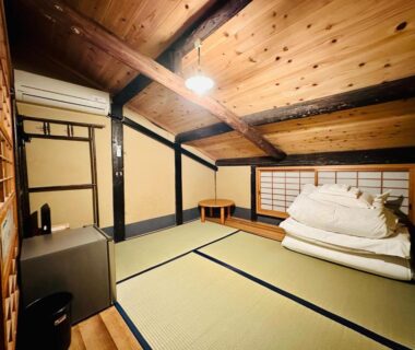 Traditional tatami room with stacked futons, shoji screens and exposed wooden beams at Nagomi-Ryokan Yuu in Kyoto