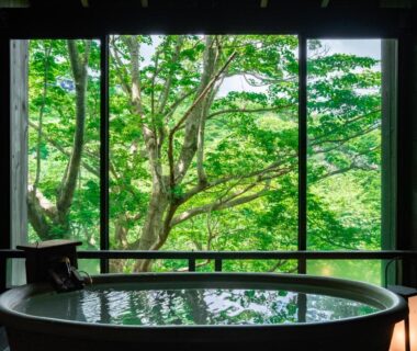 Indoor wooden bathtub beside large window overlooking lush green trees at Nagominoyado Hanagokoro in Kanagawa