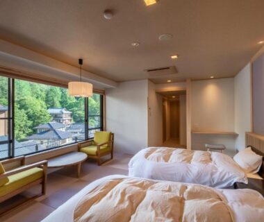 Twin beds and seating area at Nakamatsuya Ryokan overlooking greenery and nearby buildings in Nagano, Chūbu