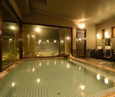 Spacious indoor tiled onsen bath with shower stations and large viewing window at Nakamatsuya Ryokan, Nagano