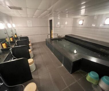 Indoor communal onsen area with long rectangular bath, washing stations, stools and shower faucets at Nakamuraya Ryokan